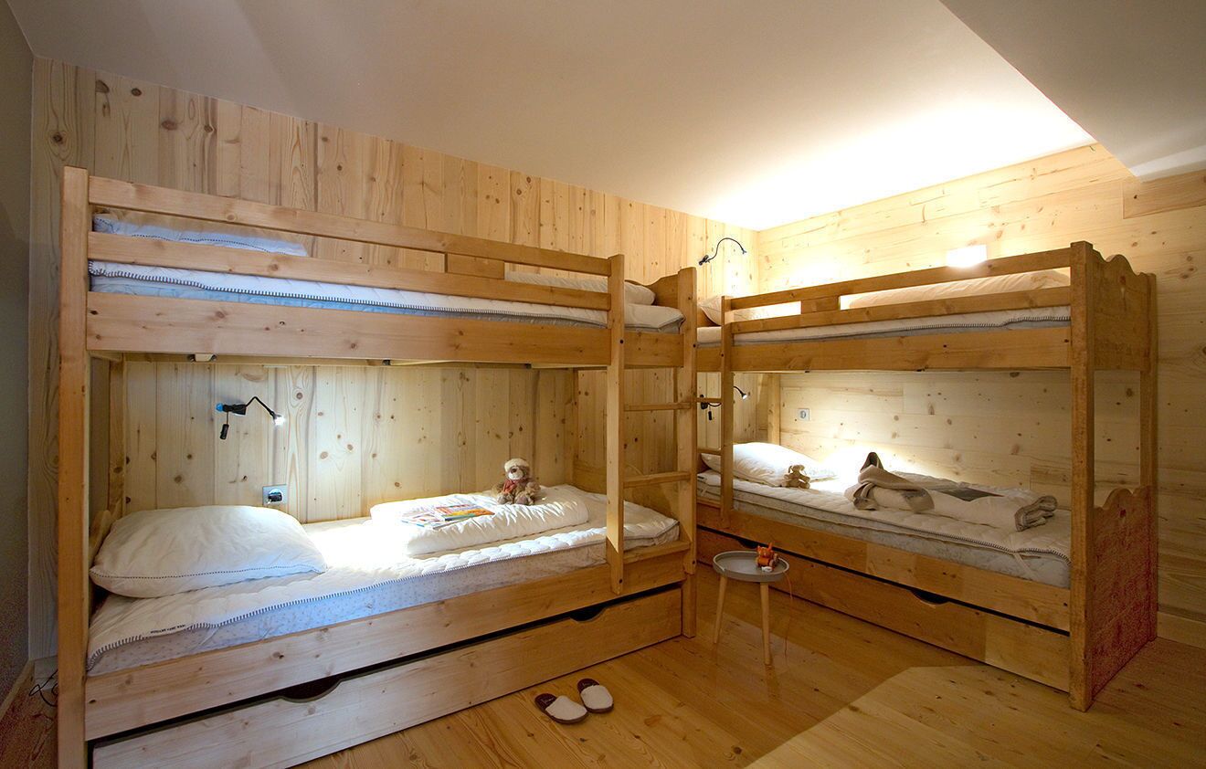 Et værelse med køjeseng i træ, et lille bord og et par slippers på gulvet.