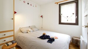A bedroom with a bed, pillows, a hanging heart decoration, a window with heart stickers, and a small stool. - Près du Télémixte du Diable |  T2 moderne + vue (Les Deux Alpes)