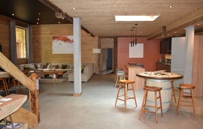 Un vaste espace de vie comprenant un grand canapé, des éléments décoratifs en bois, une cuisine avec des tabourets et un coin bar.