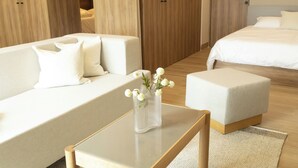 A modern hotel room with a sofa, a small table with a vase of flowers, a bed, and wooden wardrobes. - Margot. Expo (Guadalajara)