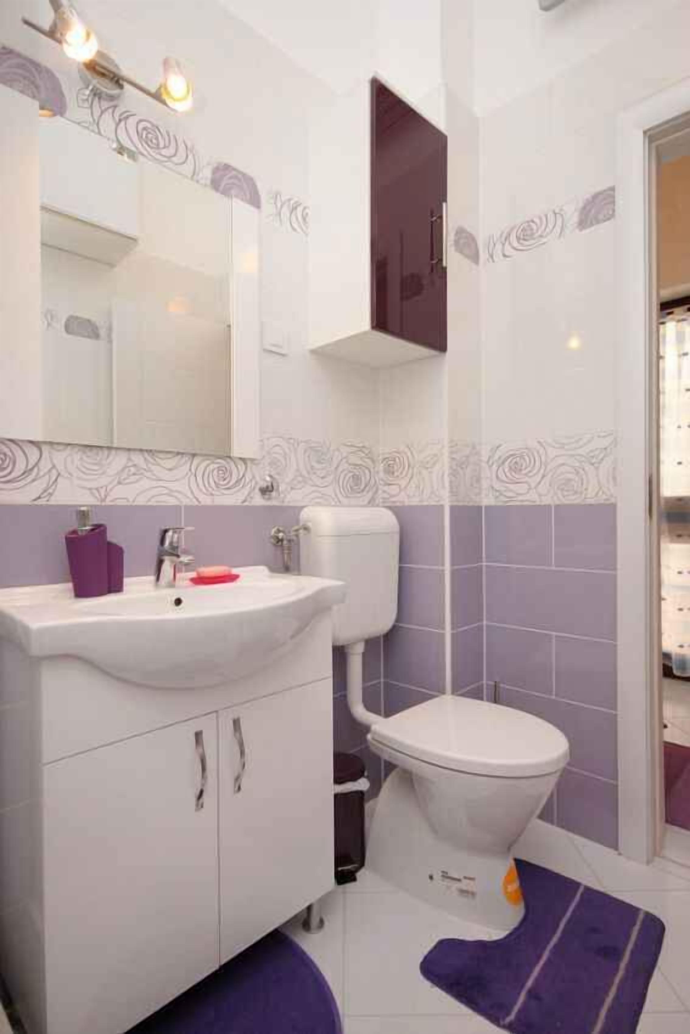 A bathroom with a white sink, purple tiles, a white toilet, and a purple rug.