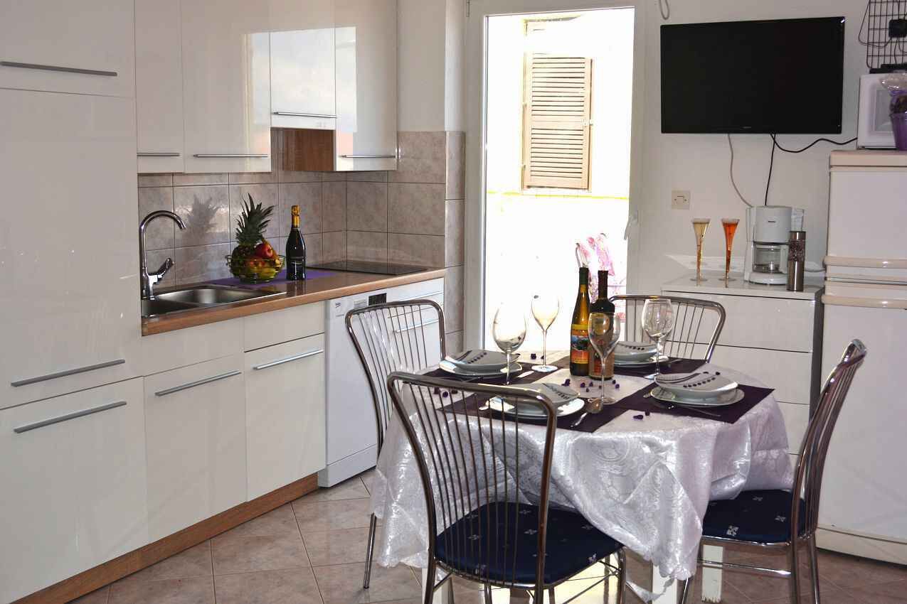 Een kleine keuken met witte kastjes, een gootsteen en een eethoek met een tafel gedekt voor twee personen.