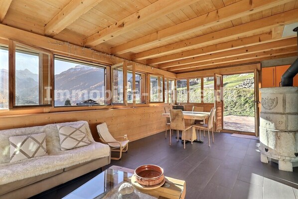 A wooden cabin with a sofa, dining table, chairs, and a fireplace.