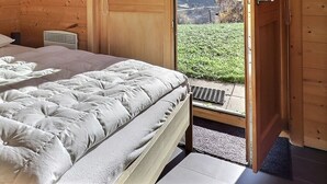 Ein Schlafzimmer einer Holzhütte mit einem Bett, Kissen, einem Nachttisch und einem Fenster mit Ausblick.