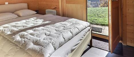 Un dormitorio de cabaña de madera con cama, almohadas, mesita de noche y ventana con vistas.