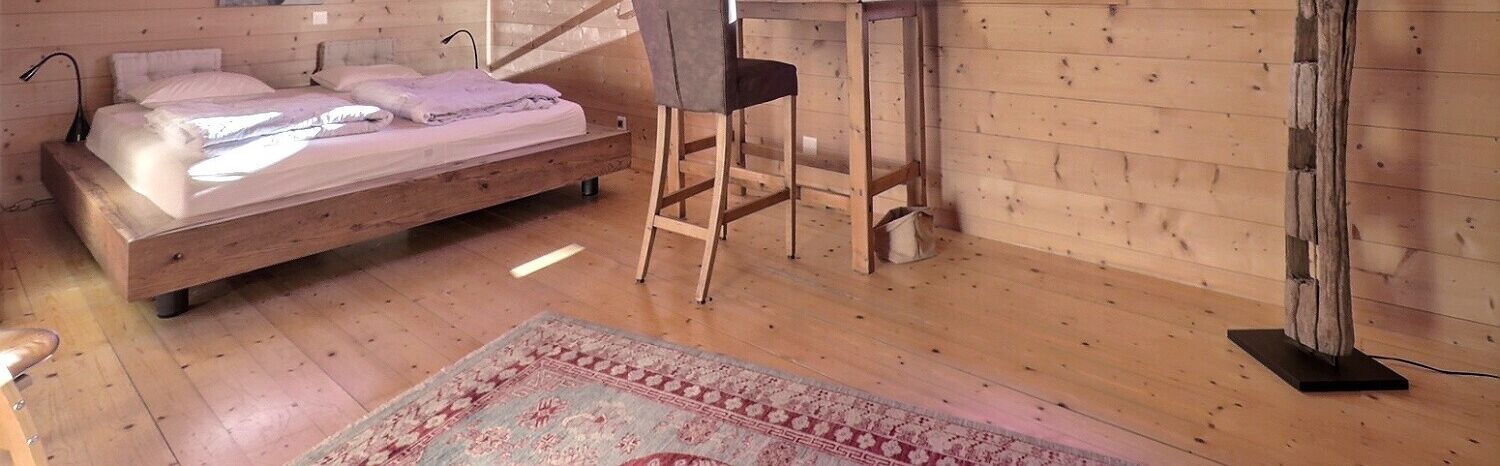 A wooden-paneled room with a bed, a chair, and a rug.