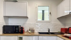 Eine moderne Küche mit weißen Schränken, einer Mikrowelle, einer roten Kaffeemaschine, einem Spülbecken und einem Fenster mit Blick auf Grünflächen.