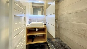 Ein modernes Badezimmer mit einer Duschkabine aus Glas, einem weißen Waschbecken und einem Spiegel darüber.