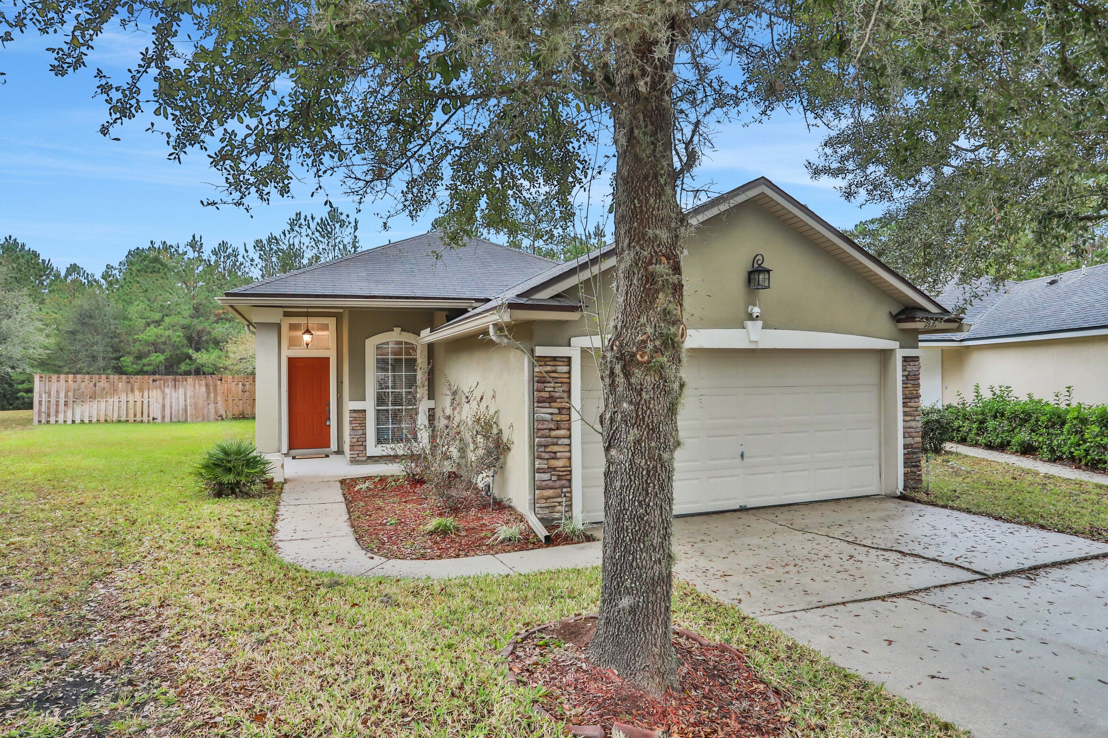 A single-story house with a garage, a front yard with a tree, and a wooden fence in the background.