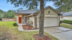 A single-story house with a garage, a front yard with a tree, and a wooden fence in the background. - ~Spacious 4/2 in Oakleaf, pet friendly (Orange Park)