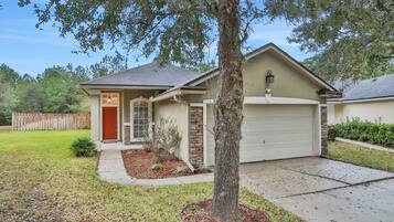 A single-story house with a garage, a front yard with a tree, and a wooden fence in the background.