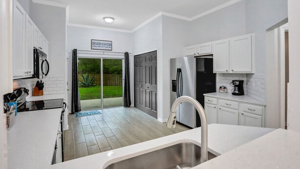A modern kitchen with white cabinets, a stainless steel sink, and a black refrigerator. - ~Spacious 4/2 in Oakleaf, pet friendly (Orange Park)
