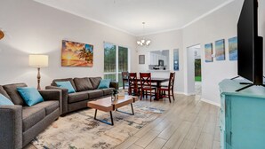 A living room with a sofa, coffee table, and a TV. There is a dining area with a table and chairs. - ~Spacious 4/2 in Oakleaf, pet friendly (Orange Park)