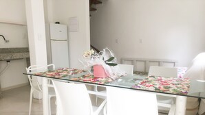 Un comedor con mesa de vidrio, sillas blancas y mantel con estampado floral.