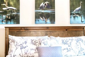 A bedroom with a wooden headboard, floral bedding, and three wall-mounted bird paintings. - Stunning Beach Front Suite 15min To Downtown! (Victoria)