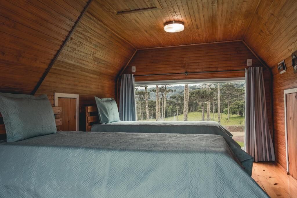 Quarto com duas camas, teto de madeira e janela com cortinas.