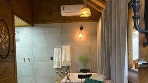 Una habitación acogedora de estilo cabaña con techo de madera, un banco empotrado, una butaca con cojín, una mesita y un calentador fijado a la pared.