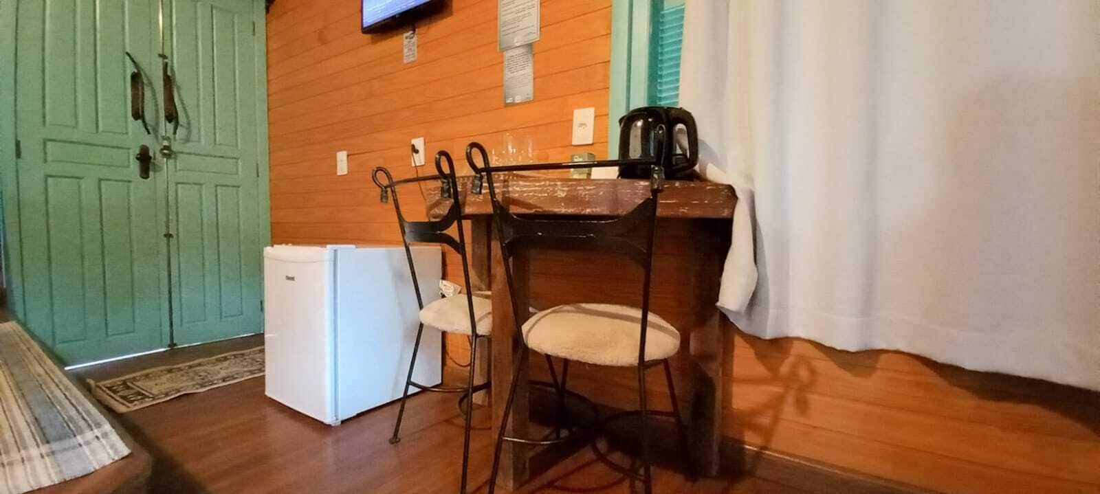 Une petite cuisine équipée d’un réfrigérateur, d’un évier et d’une cuisinière. On y trouve une table en bois avec des chaises et un rideau blanc.