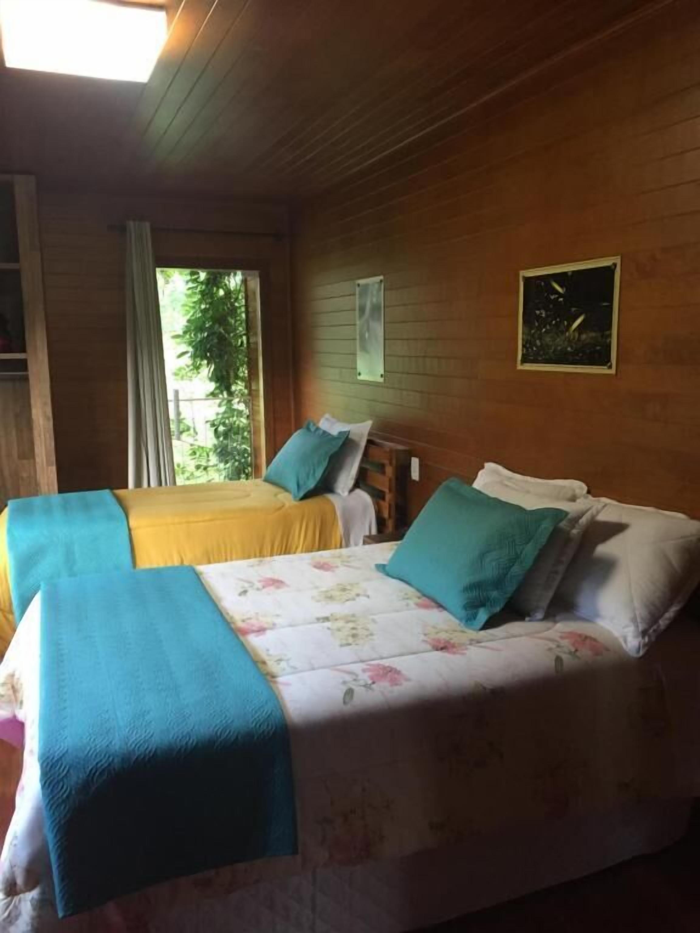 A room with two beds, a wooden ceiling, and a window with a view of greenery.