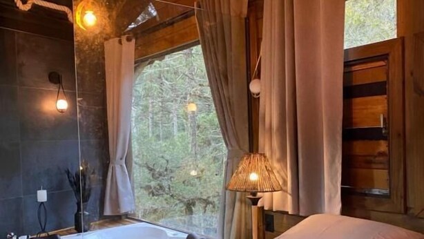 Un dormitorio acogedor con una cama grande, una zona de estar y vistas al bosque a través de una ventana.