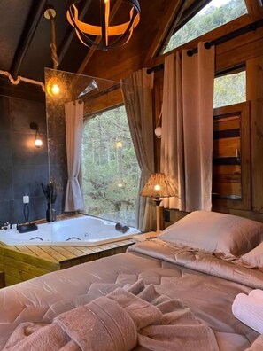 A cozy bedroom with a large bed, a sitting area, and a view of the forest through a window. - Eco Pousada Invernador (Urubici)