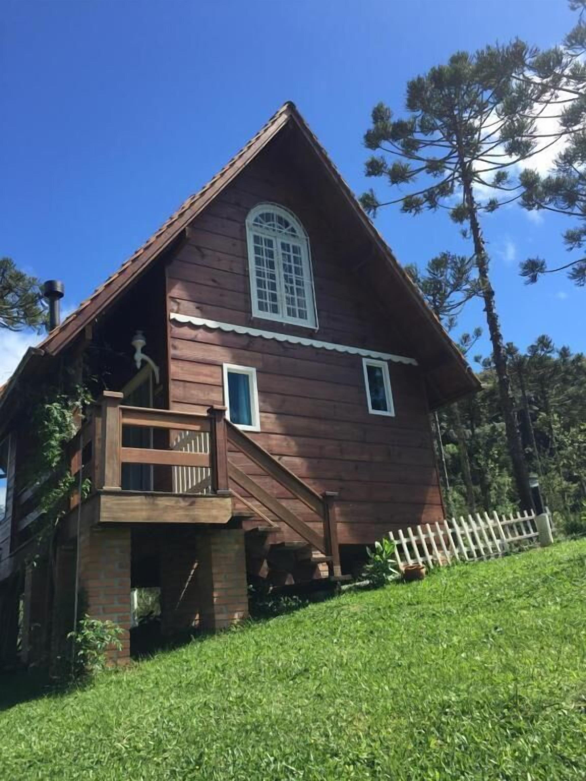 A wooden cabin with a balcony, a chimney, and a white picket fence.