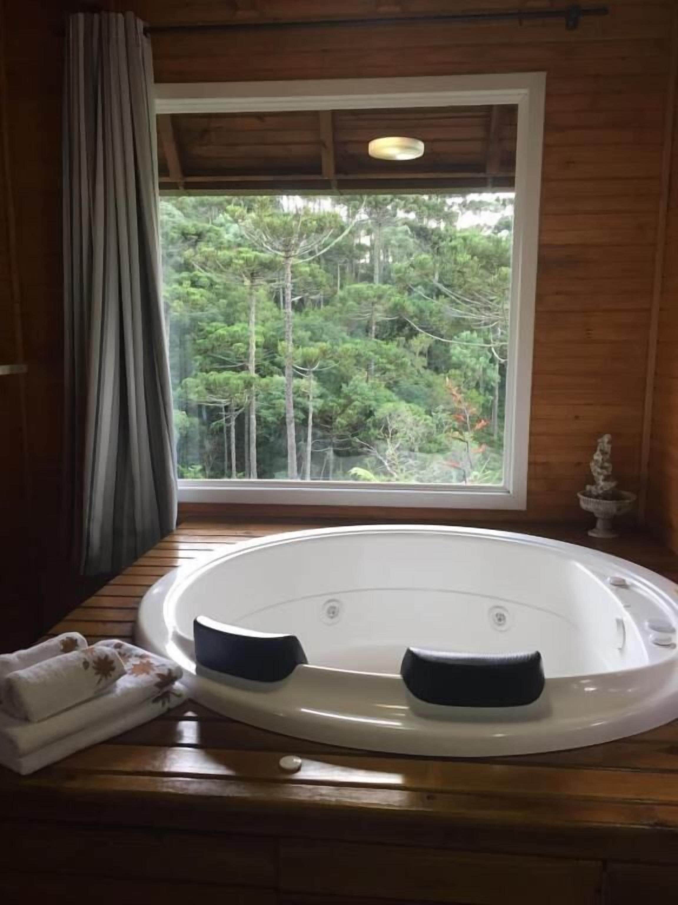 Uma cabana de madeira com uma janela grande, uma banheira de hidromassagem e uma pequena estátua.