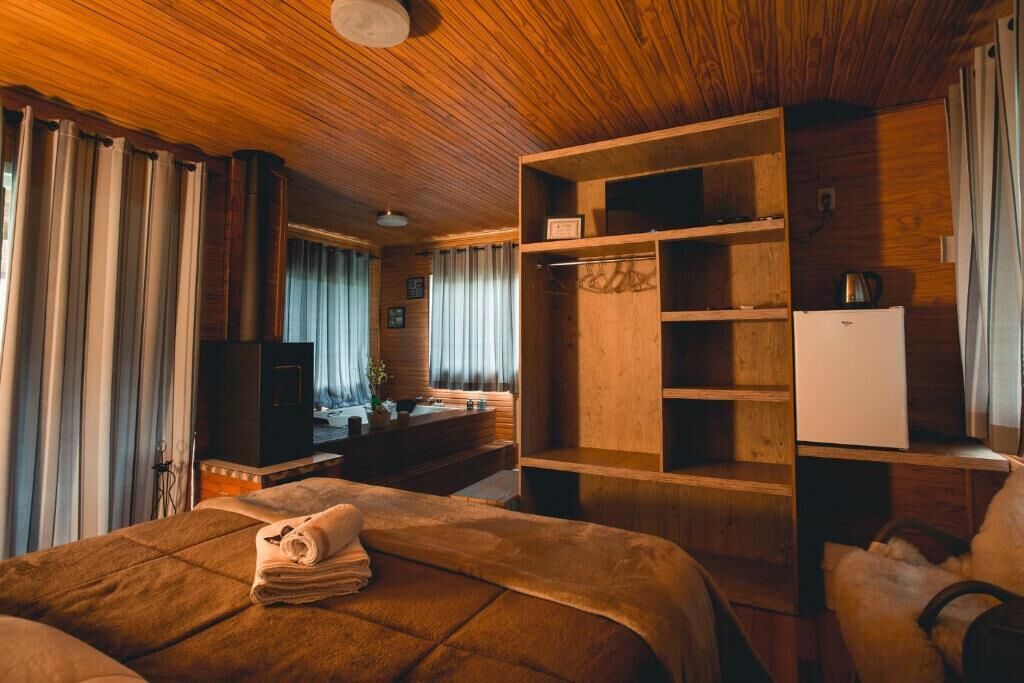 A wooden-paneled room with a bed, a desk, a television, and a refrigerator.