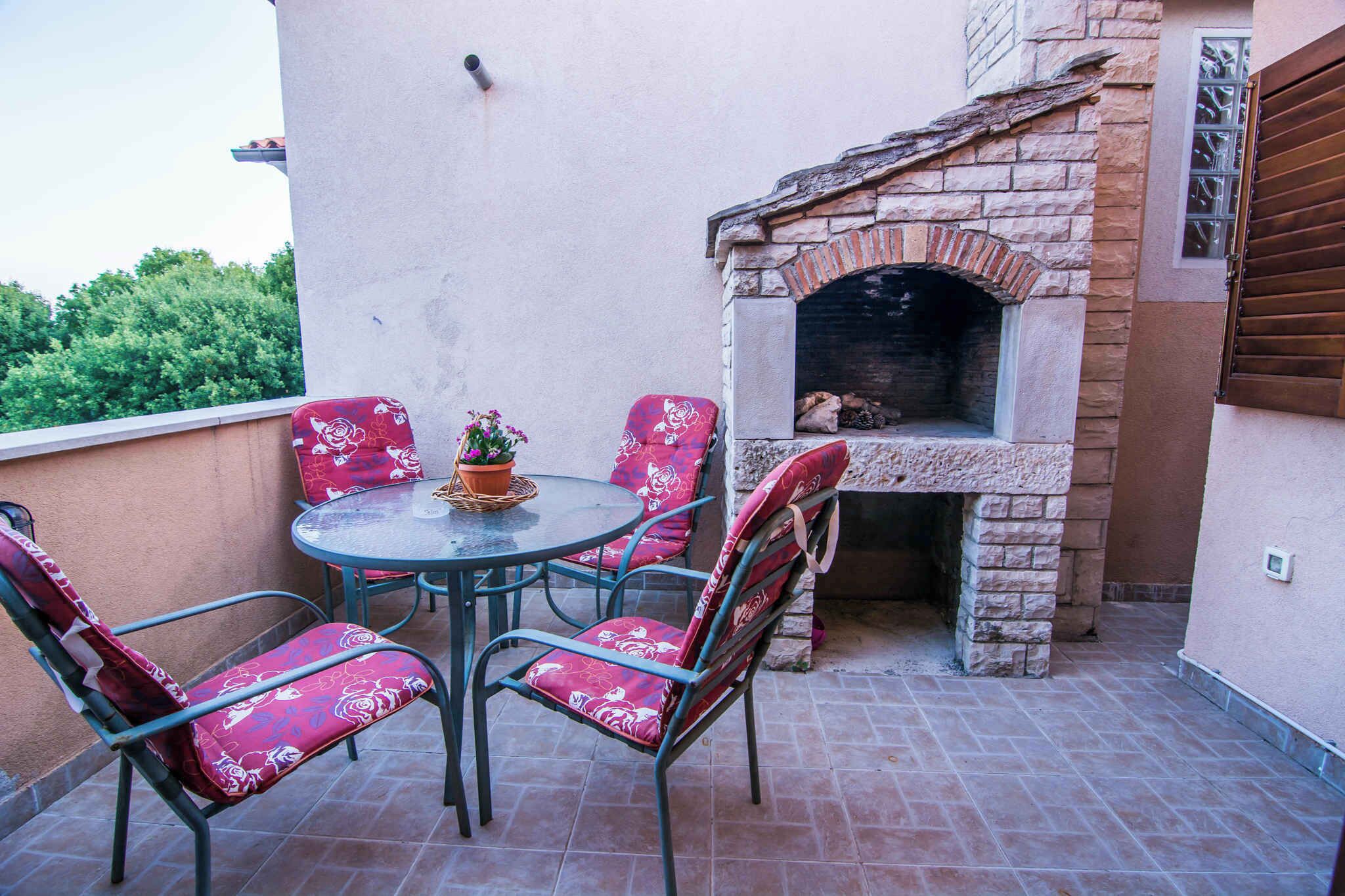 A patio with a round table and four chairs, a stone-built outdoor oven, and a potted plant.