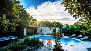 Una piscina con sillones de descanso, un jacuzzi y senderos de piedra.