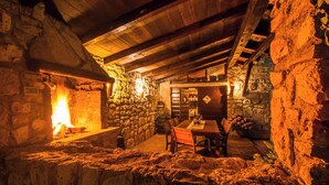 Interior rústico de piedra con chimenea, vigas de madera y zona de comedor.