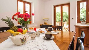 A dining area with a wooden table set for breakfast, including fruits, a teapot, and cups.