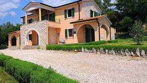 A two-story house with a stone facade, green shutters, and a gravel driveway.