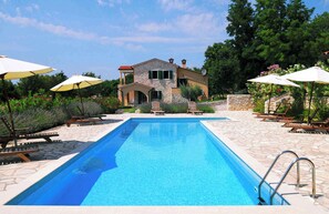 Relax by the serene pool surrounded by lush gardens and a charming stone building.