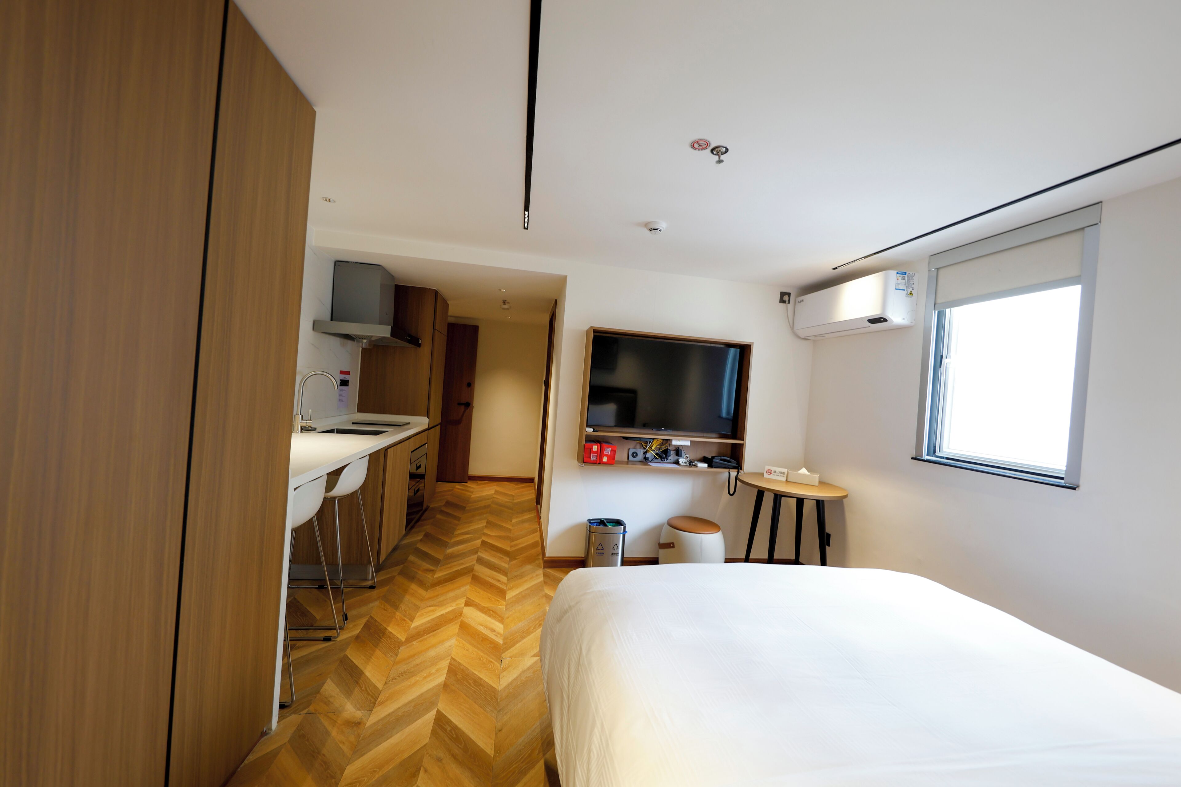 Habitación de hotel con cama, televisor montado en la pared, escritorio pequeño y kitchenette.