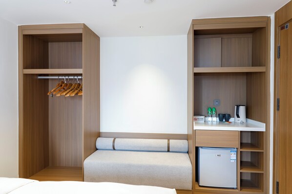 A hotel room with a built-in wardrobe, a seating area, a kitchenette, and a small refrigerator.