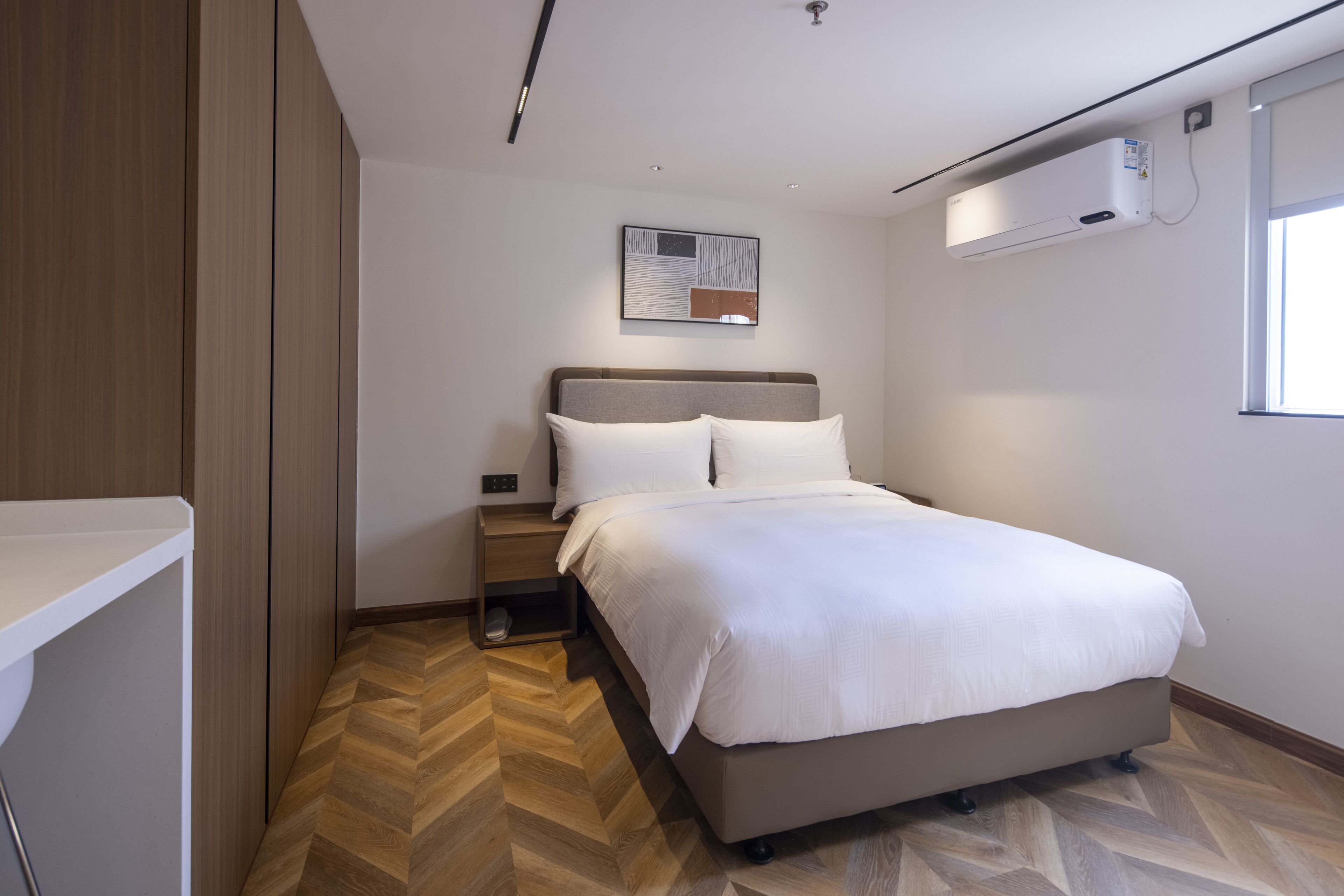 Une chambre d’hôtel moderne équipée d’un lit, d’une table de chevet et d’un climatiseur fixé au mur.