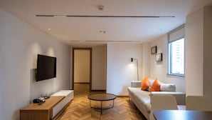 A modern living room with a flat-screen TV, a wooden bench, a round coffee table, a sofa with orange cushions, and a large window. - LN Residece Taojin (Guangzhou)