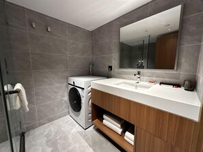 A modern bathroom with grey tiles, a washing machine, a large mirror, and a wooden vanity. - LN Residece Taojin (Guangzhou)