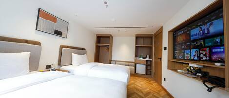 A hotel room with two beds, a TV mounted on the wall, and a wooden floor.