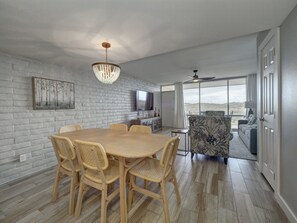 A spacious dining area with a wooden table and wicker chairs, a television, and a view of the outdoors through large windows. - Beautiful view of the beach from the balcony, newly remodeled with new furniture (Port Aransas)
