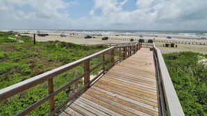 Une promenade en bois menant à une plage, avec un ciel dégagé et quelques nuages.