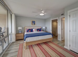 A bedroom with a bed, nightstands, a ceiling fan, and a window with a view. - Beautiful view of the beach from the balcony, newly remodeled with new furniture (Port Aransas)