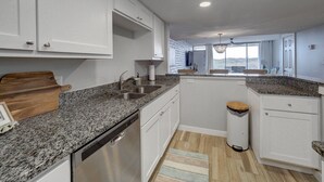 Une cuisine moderne avec des armoires blanches, des comptoirs en granit, un lave-vaisselle et une vue sur l’extérieur.
