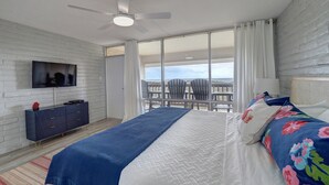 Une chambre avec un lit, une télévision, une commode et un balcon avec des chaises.