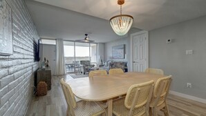 Un vaste espace dédié à la salle à manger, avec une table en bois et des chaises en osier, un lustre et une vue dégagée grâce à de grandes fenêtres.