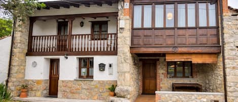 A two-story stone house with a balcony, a fireplace, and a small outdoor seating area.
