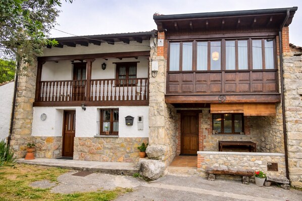 A two-story stone house with a balcony, a fireplace, and a small outdoor seating area.
