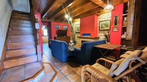 Een knus interieur met een trap, blauwe banken, een open haard en rieten meubels.