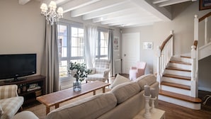 Een woonkamer met televisie, bank, fauteuil en een trap.